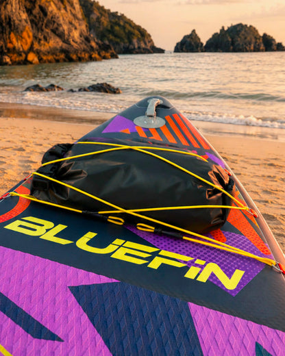 Inflatable paddleboard on sandy beach with black dry bag and colorful graphics at sunset