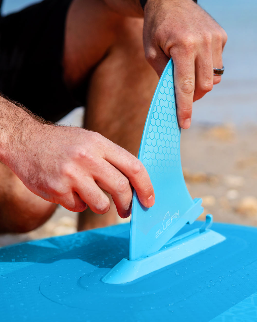 person attaching a blue smartlock fin on a beach