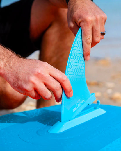 person attaching a blue smartlock fin on a beach